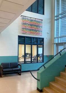 A wall hanging made of bright colored beads hangs over an office window.