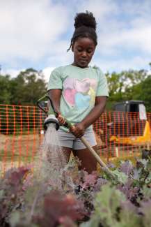 a child using a hose to spray water on plants